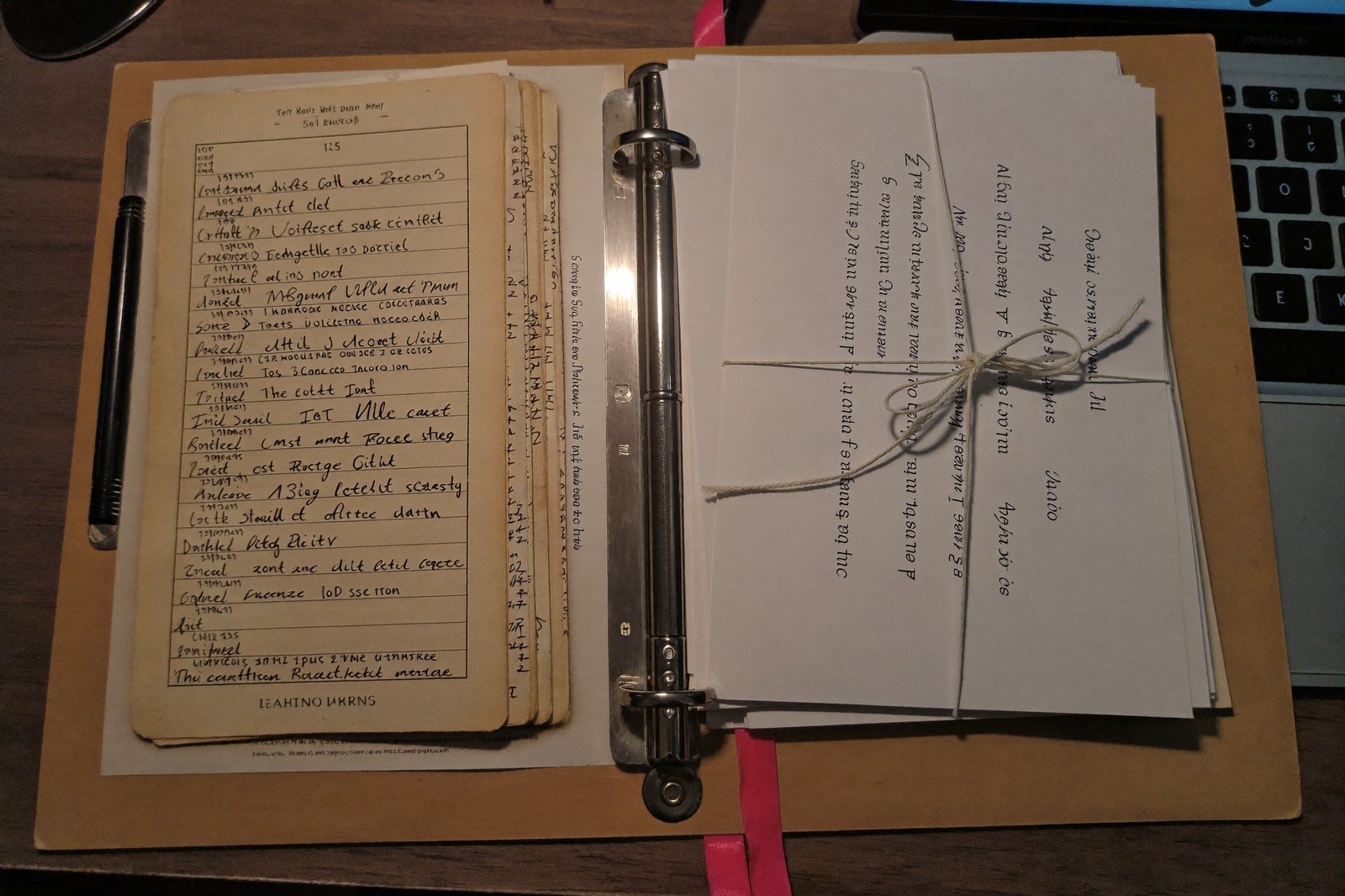 A vintage rolodex and a bundle of letters on a wooden desk beside a glowing laptop, evening light