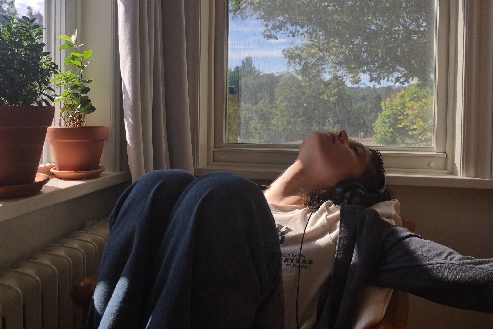 A person relaxing in a window seat with headphones on, eyes closed, morning light, the feeling a product sells
