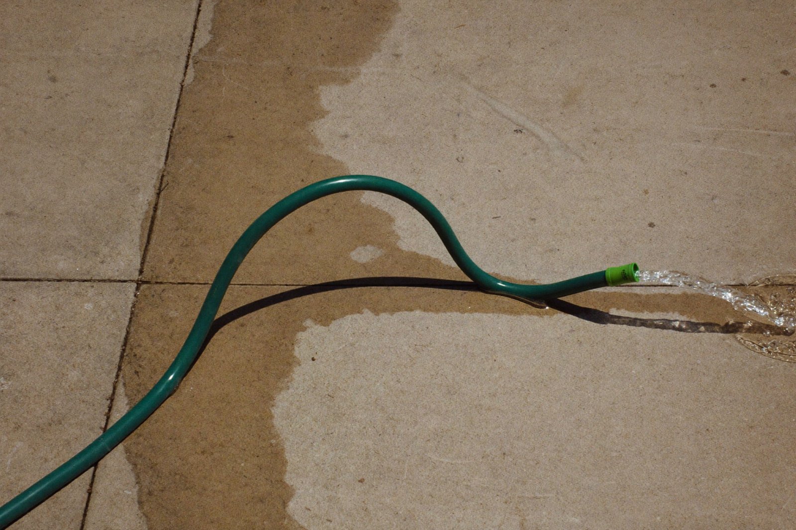 A garden hose with a sharp kink in it lying on a sunlit driveway, water pooling behind the bend