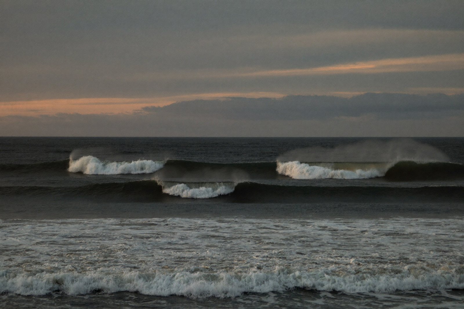 Ocean waves at four stages, building, cresting, breaking and receding, under a wide evening sky