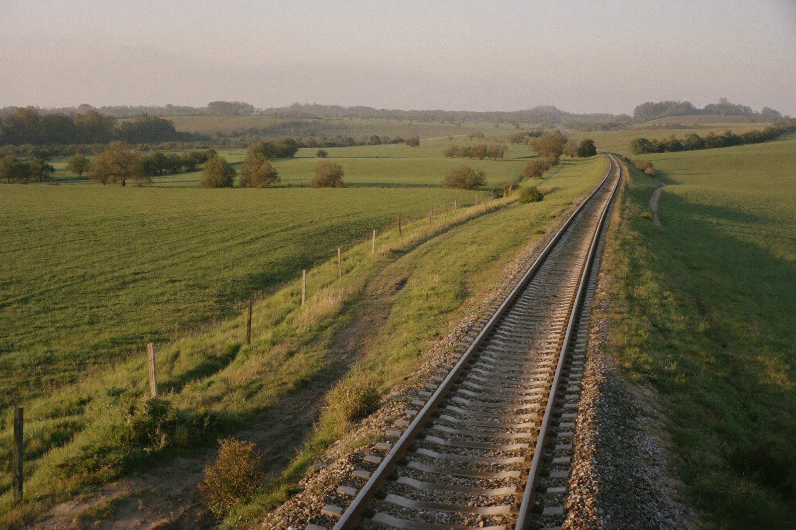 Two railway tracks diverging in different directions across open country at golden hour