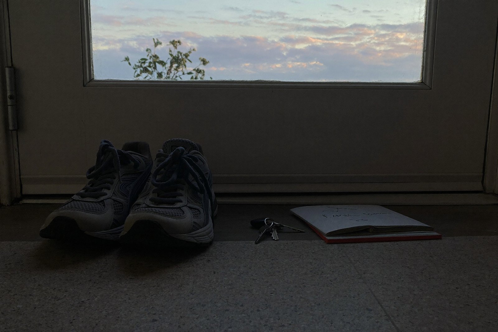 A single pair of running shoes by a front door at dawn, keys and a folded note beside them