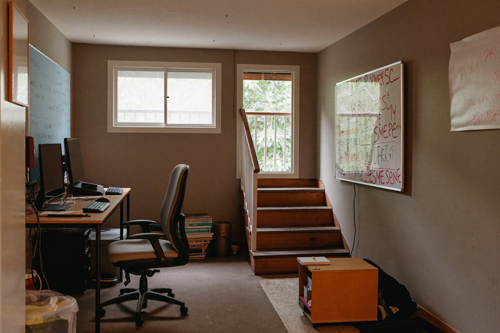 A basement office with two desks, a whiteboard of sketches, and a staircase leading up